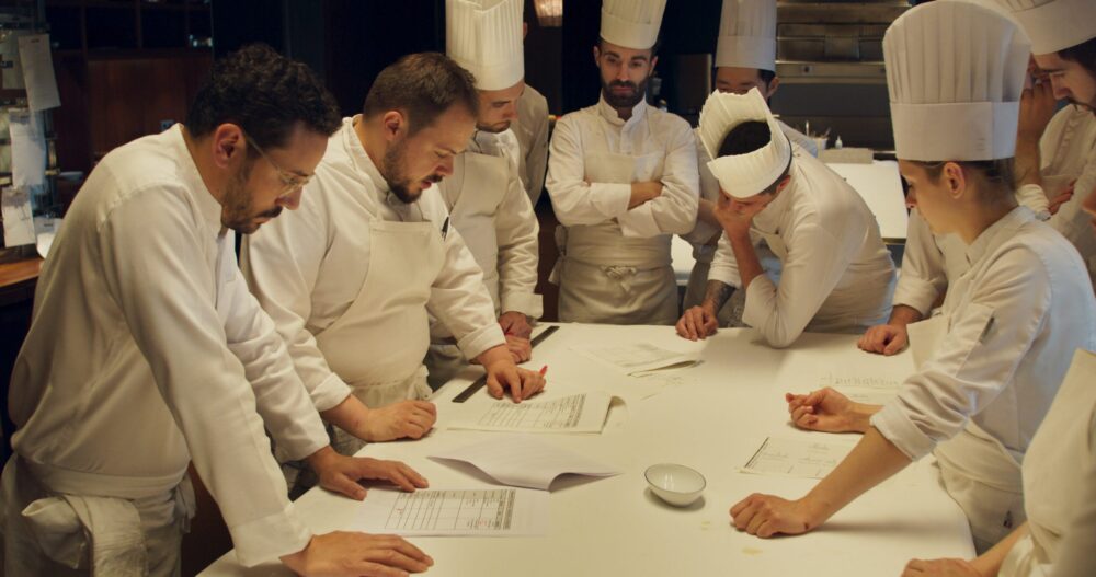 Chefs in whites reviewing menus at Les Troisgros, a restaurant featured in Menus-Plaisirs.