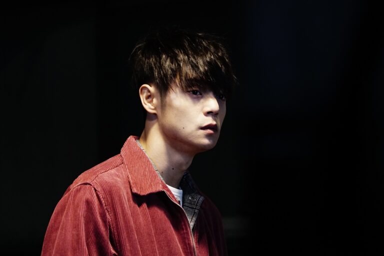 Brooding young man with dark hair, wearing a red corduroy jacket.