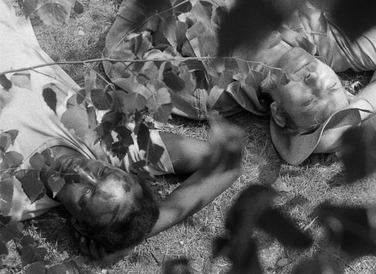 Still from Sudanese Film Group shorts, showing two men lying on the ground, one Black and one white.