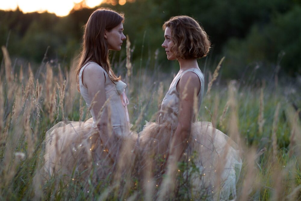 Two women in tulle dresses face each other in a field.