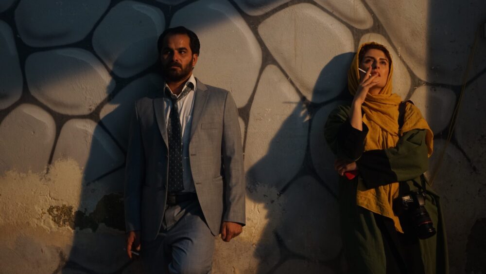 Man and woman smoking by a graffiti wall in Tehran.