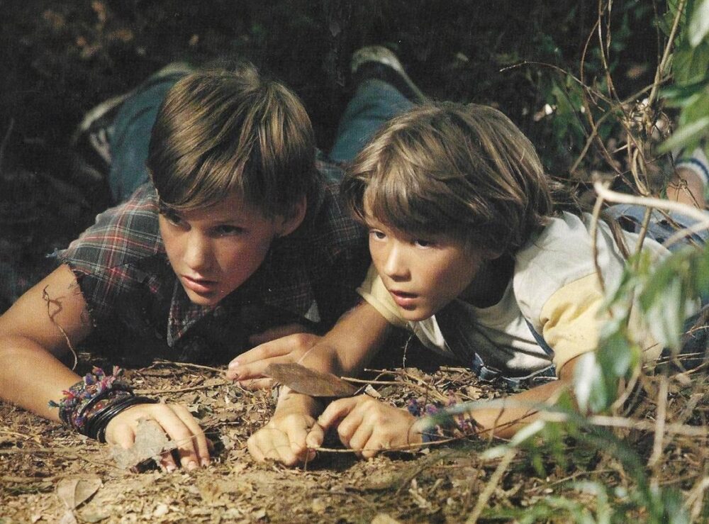 Two young boys lying in the dirt, exploring nature.