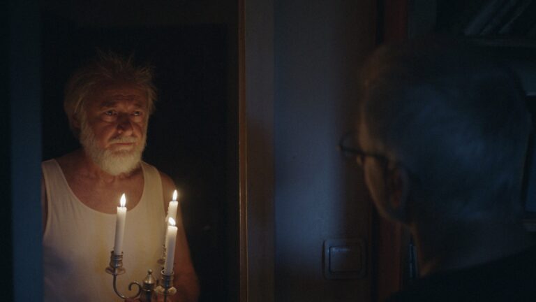 Man in tank top with candles, reflecting in mirror, reminiscent of the film "The Father