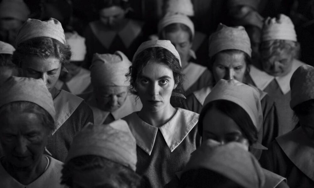 Black and white image of a woman surrounded by other women in uniform caps and collars.