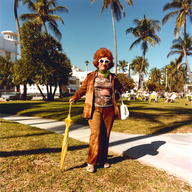 Woman in 1970s attire poses in a sunny park with palm trees.