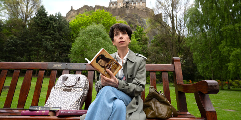 Woman reading "The Lost King" book on a bench with Edinburgh Castle in background.
