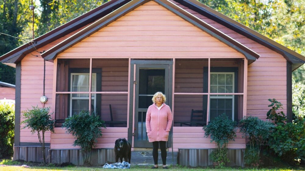 Woman and dog in front of a pink house with a screened porch.