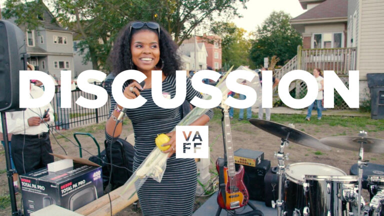 Outdoor discussion scene: Woman with microphone, band equipment, and "DISCUSSION" text overlay.