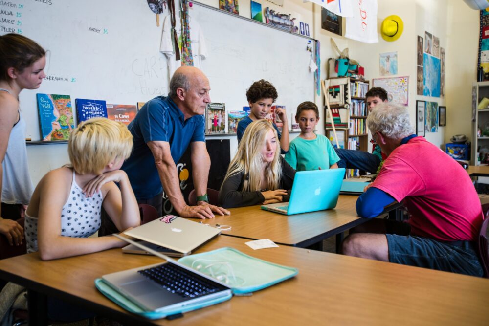 Teen Press: Students and instructors collaborate around a laptop at a table.