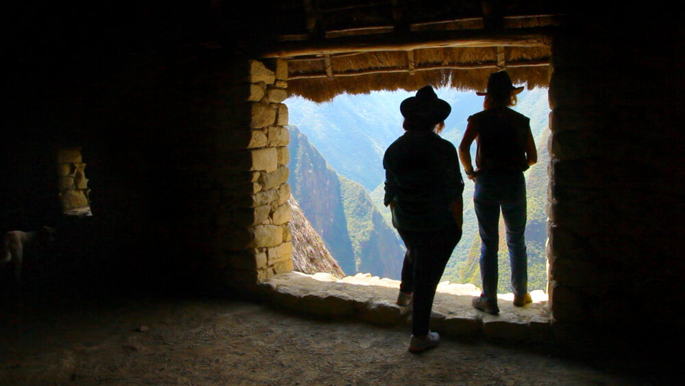 People in hats look out a stone window at a mountain view.