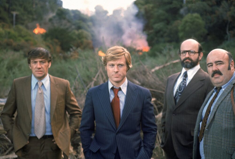Robert Redford and other actors in "The Candidate" stand in front of a burning field.