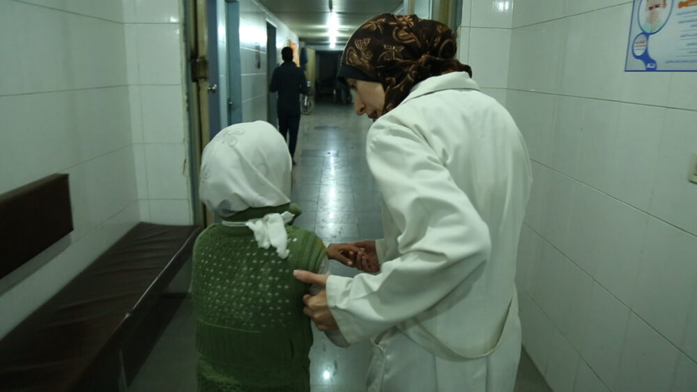 Healthcare worker examines a child in a hospital hallway.