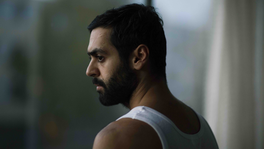 Brooding man in tank top looking out window.