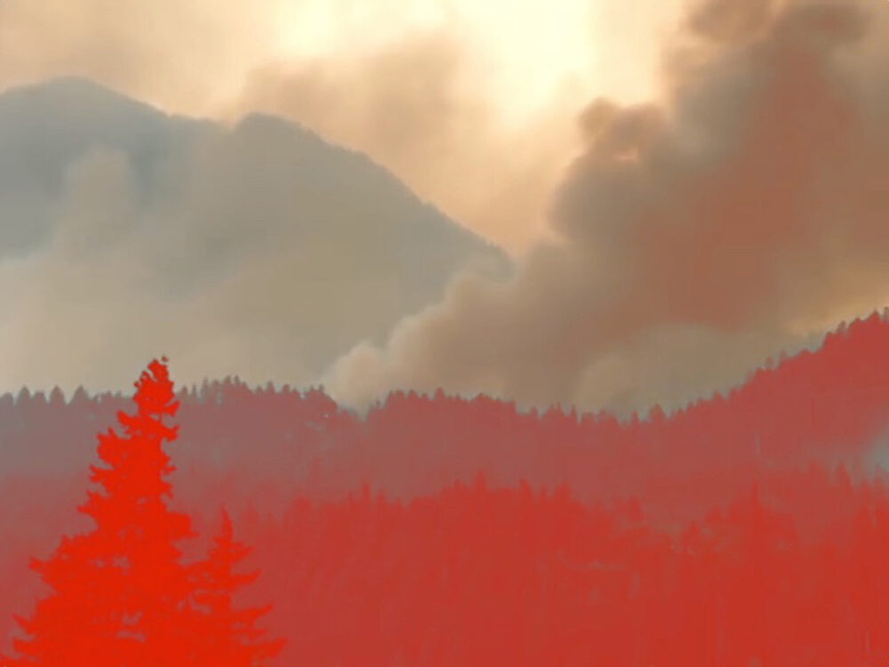 Smoke obscures mountains and forest trees, creating a hazy, fiery scene.