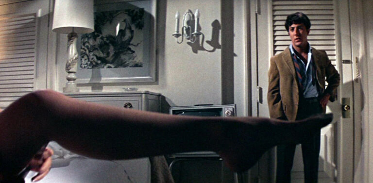 Dustin Hoffman in "The Graduate" stands in a doorway, a woman's leg in foreground.