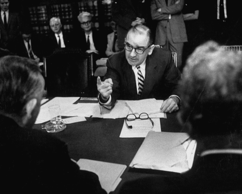 Man speaking at a table with documents.