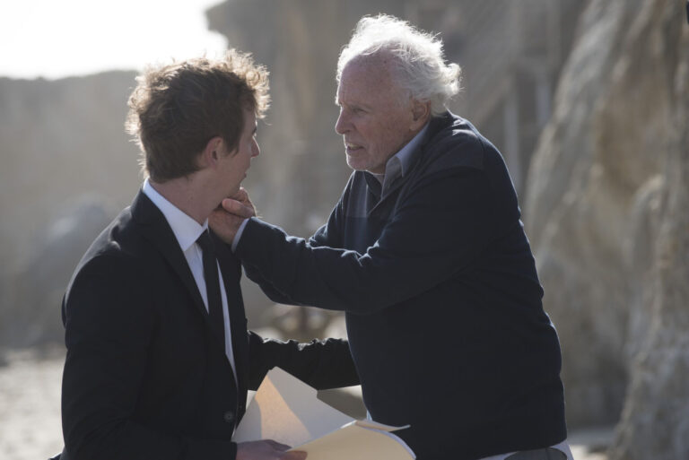 Actor Bruce Dern confronts a younger man in a suit on a beach.
