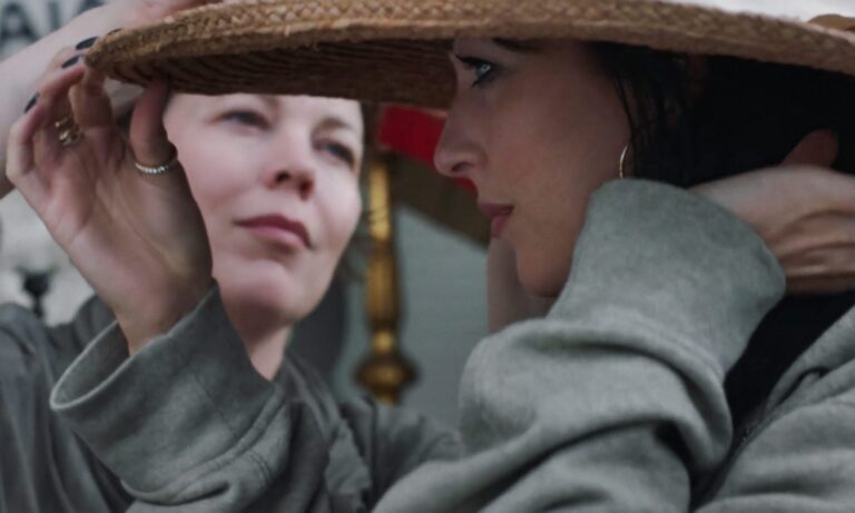 Woman fitting a straw hat on another woman.