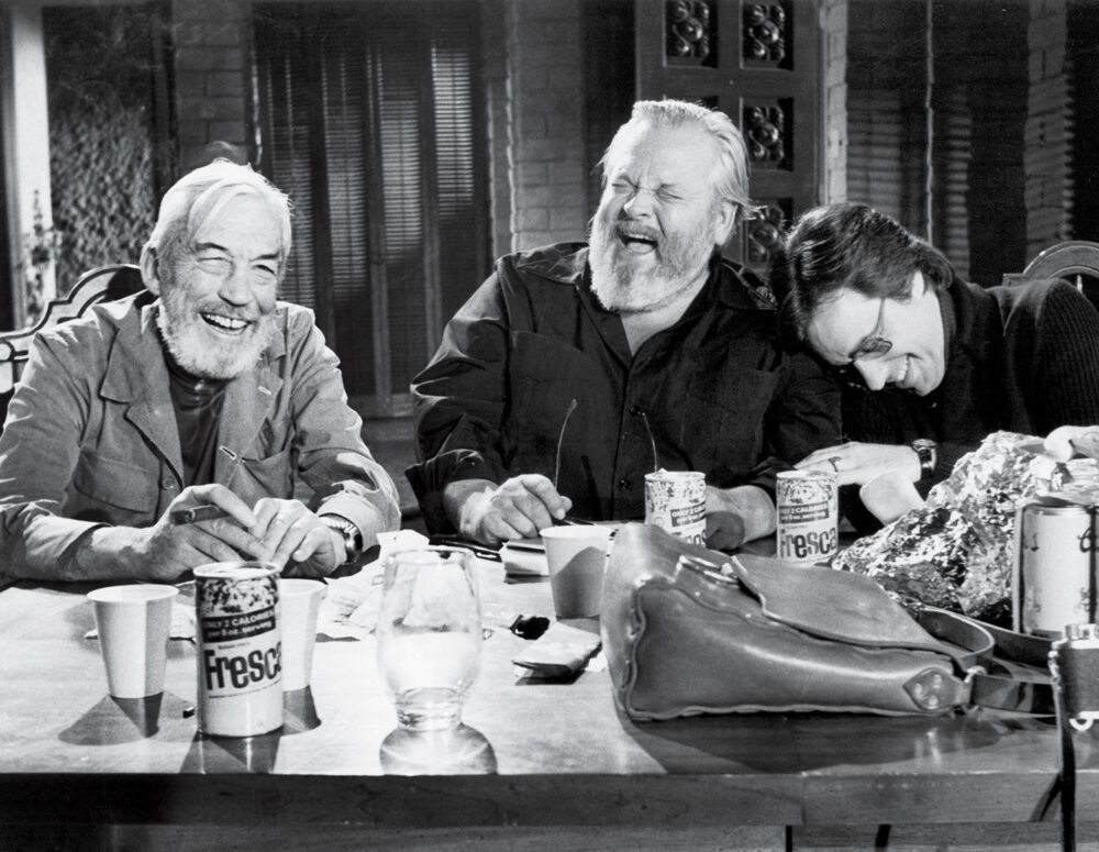 Orson Welles laughing with friends during The Other Side of the Wind filming.