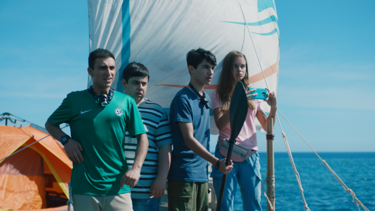 Four teenagers on a makeshift raft with a sail, orange tent visible.