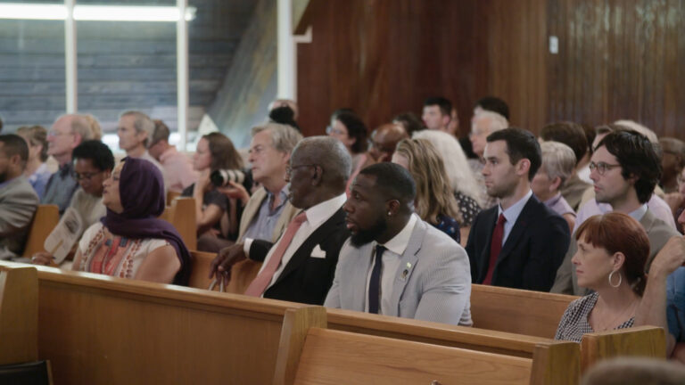 Diverse crowd seated in pews, attending an event.