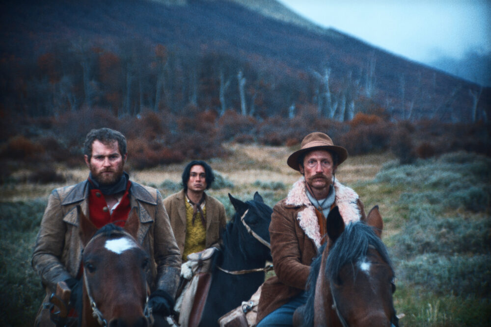 Three horsemen in "The Settlers" ride through a rugged landscape.