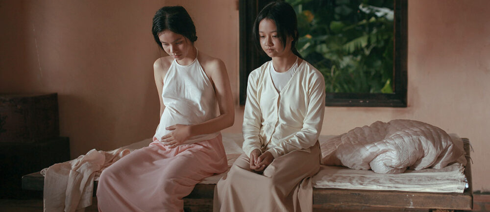 Two women sitting on a bed, one visibly pregnant, in a scene from "The Third Wife.