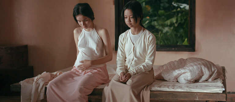 Two women sitting on a bed, one visibly pregnant, in a scene from "The Third Wife.