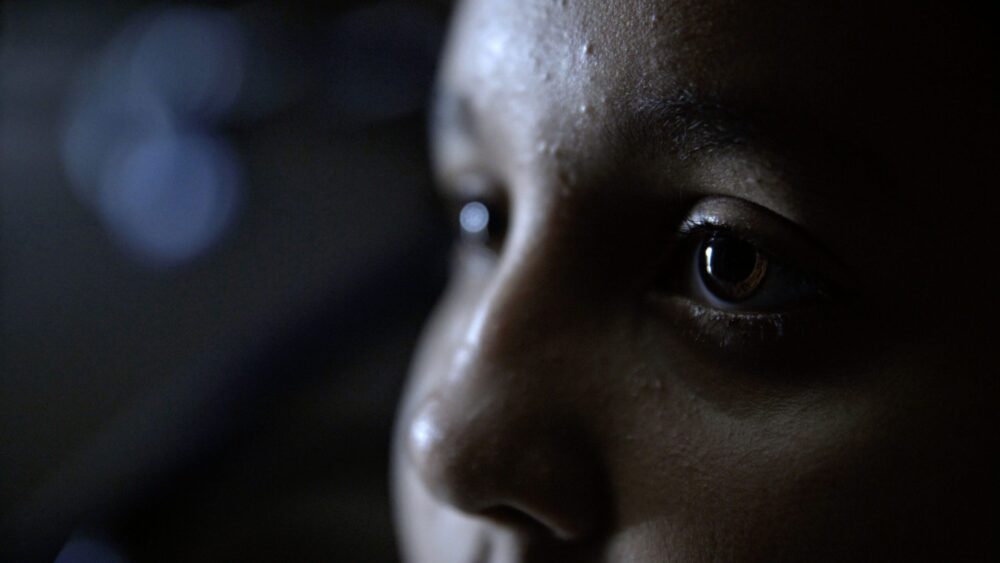 Close-up of a child's face, eyes reflecting light, possibly gazing at the sky.
