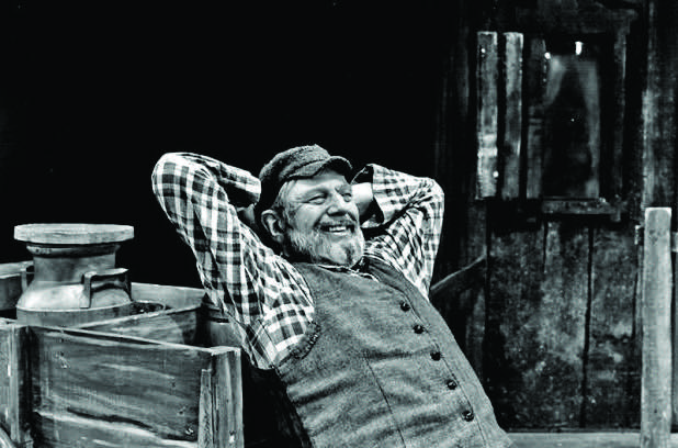 Theodore Bikel as Sholom Aleichem, smiling with hands behind his head, in a relaxed pose.