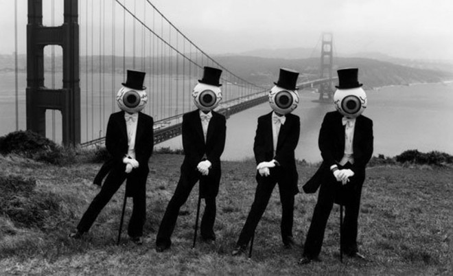 The Residents band posed in black suits, top hats, and eyeball masks in front of the Golden Gate Bridge