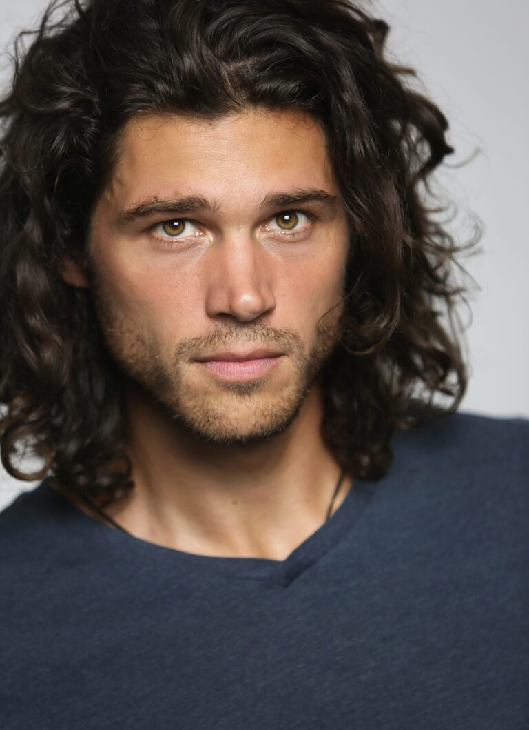 Trent Garrett headshot. Portrait of actor with long, wavy brown hair and hazel eyes.