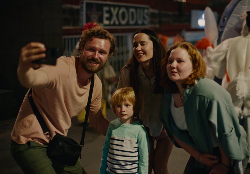 Family taking selfie under "Exodus" sign. Night scene.