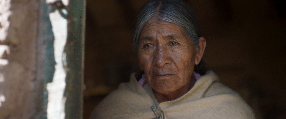 Older indigenous woman in shawl, looking thoughtful.