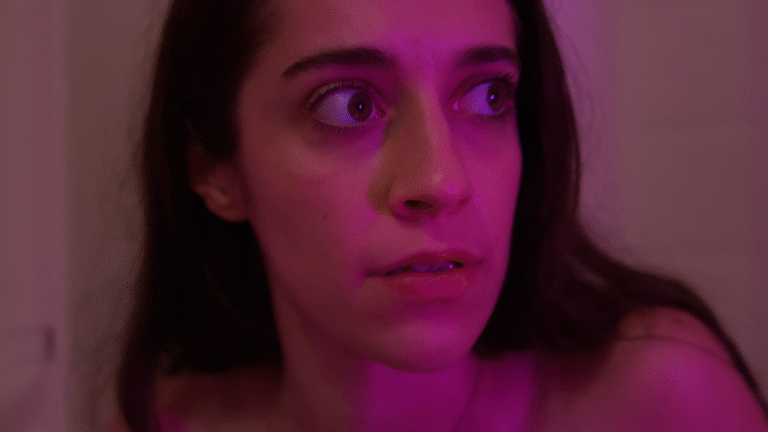 Woman with wide eyes looks anxious in pink lighting.