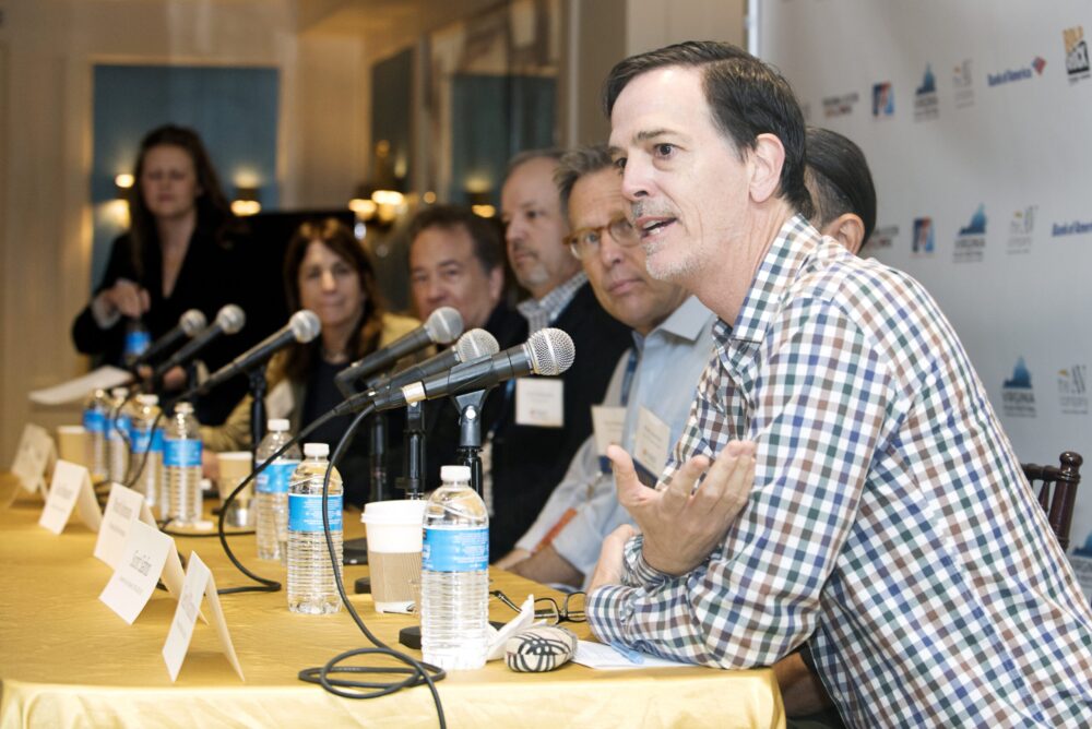 Panel discussion at Producers Forum with speakers, microphones, and water bottles.