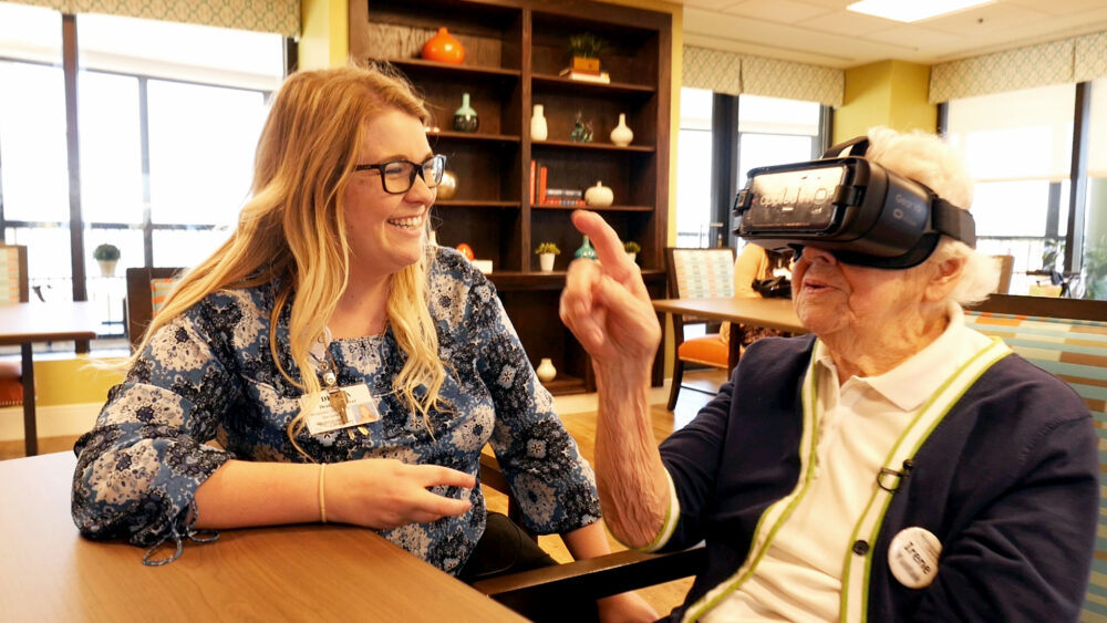 Woman with VR headset interacts with caregiver. Dementia care innovation.