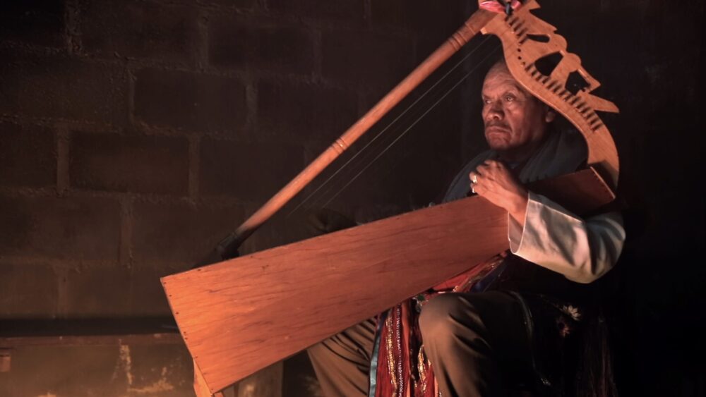 Indigenous man playing a traditional wooden harp.