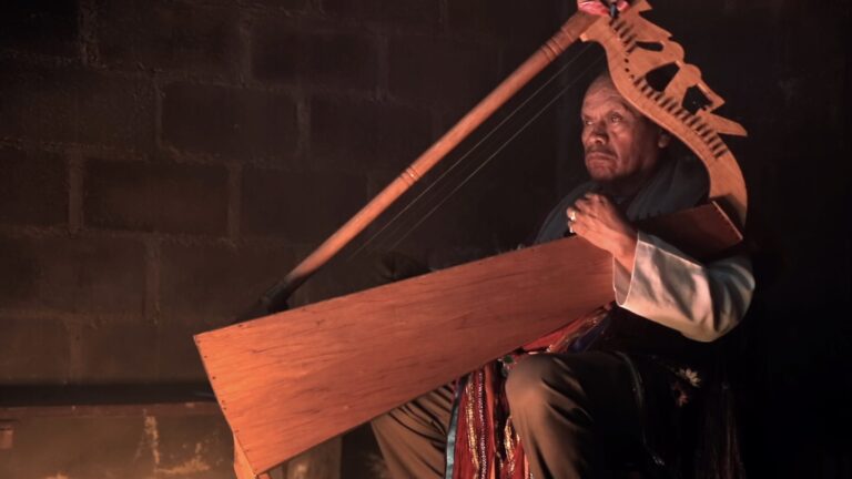 Indigenous man playing a traditional wooden harp.