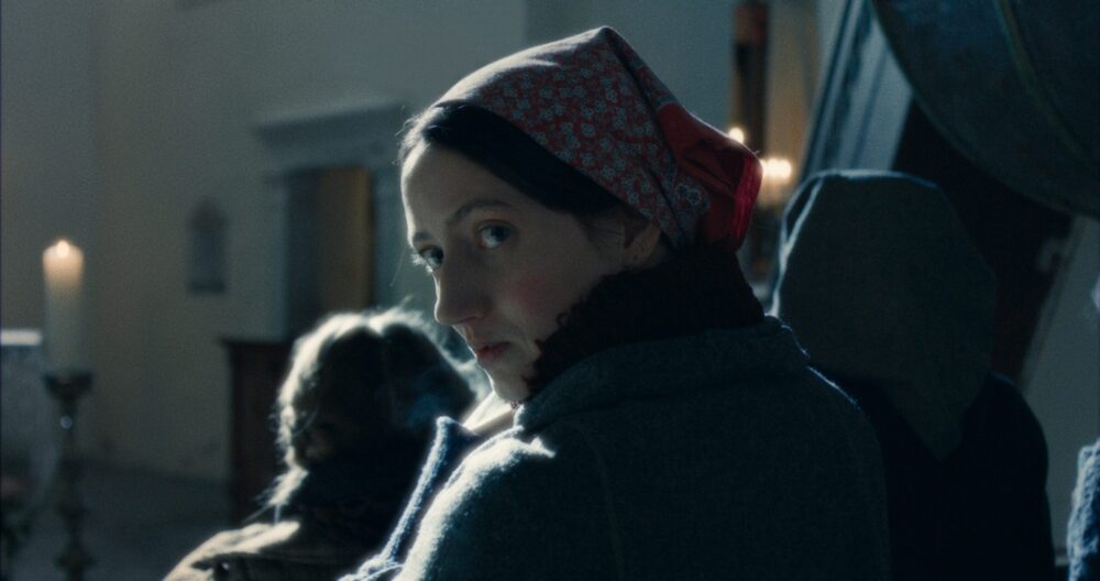 Woman in headscarf looking back in Vermiglio. Candlelight and other figures visible.