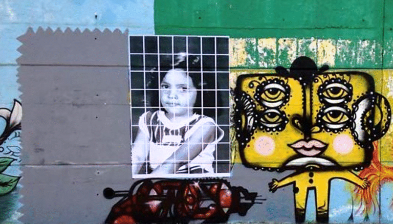 Street art featuring a child's photo overlaid with a grid, next to a stylized face with multiple eyes.