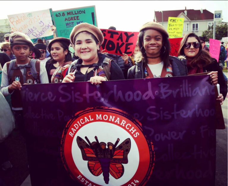Radical Monarchs at a protest, holding a banner with their logo and "Fierce Sisterhood" text.