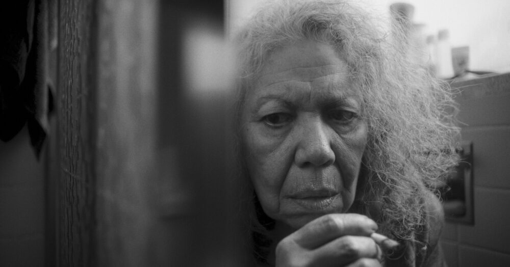 Black and white portrait of an older woman with worry in her eyes, holding a cigarette.