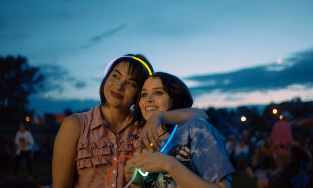 Two smiling young women with glow sticks at an outdoor event.