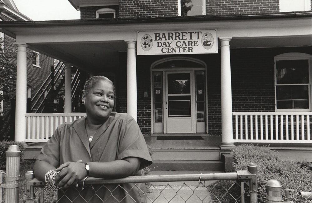 Woman in front of Barrett Day Care Center on West Main Street. Sign reads "Barrett Day Care Center.