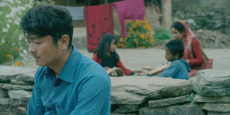 Man in blue shirt with family in background.