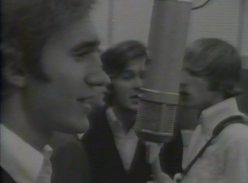 The Knickerbockers band members singing into a microphone in a studio.