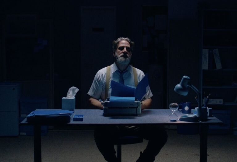 Man at typewriter in dimly lit office with blue accents