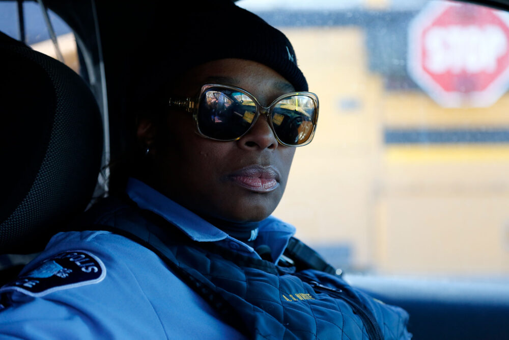 Police officer in uniform wearing sunglasses and a beanie in a patrol car.