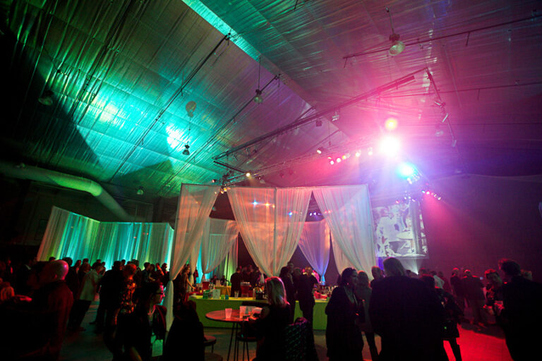 Late night wrap party with people under colorful lights in a large venue.